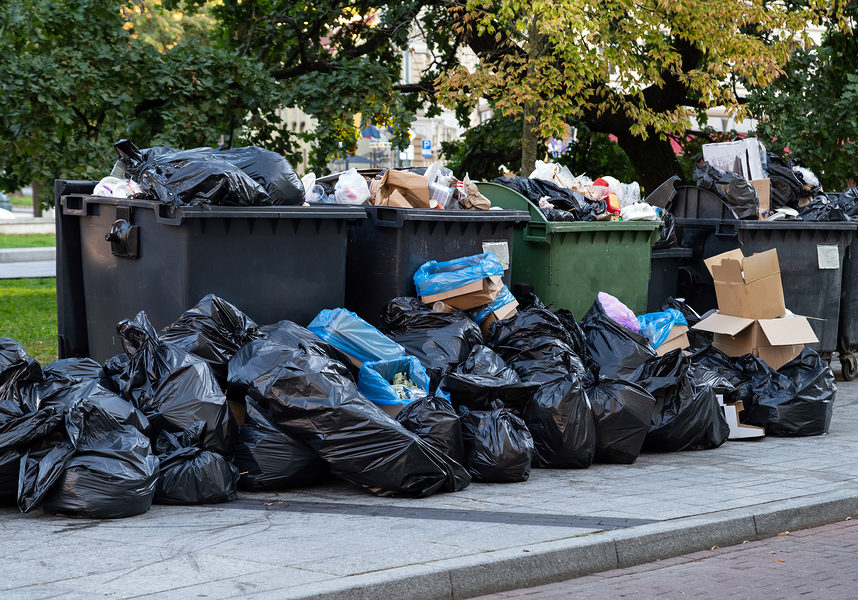 Huge garbage piles next to the dumpster after city fair. Stacks of litter bags overflow trash cans after festival in a city